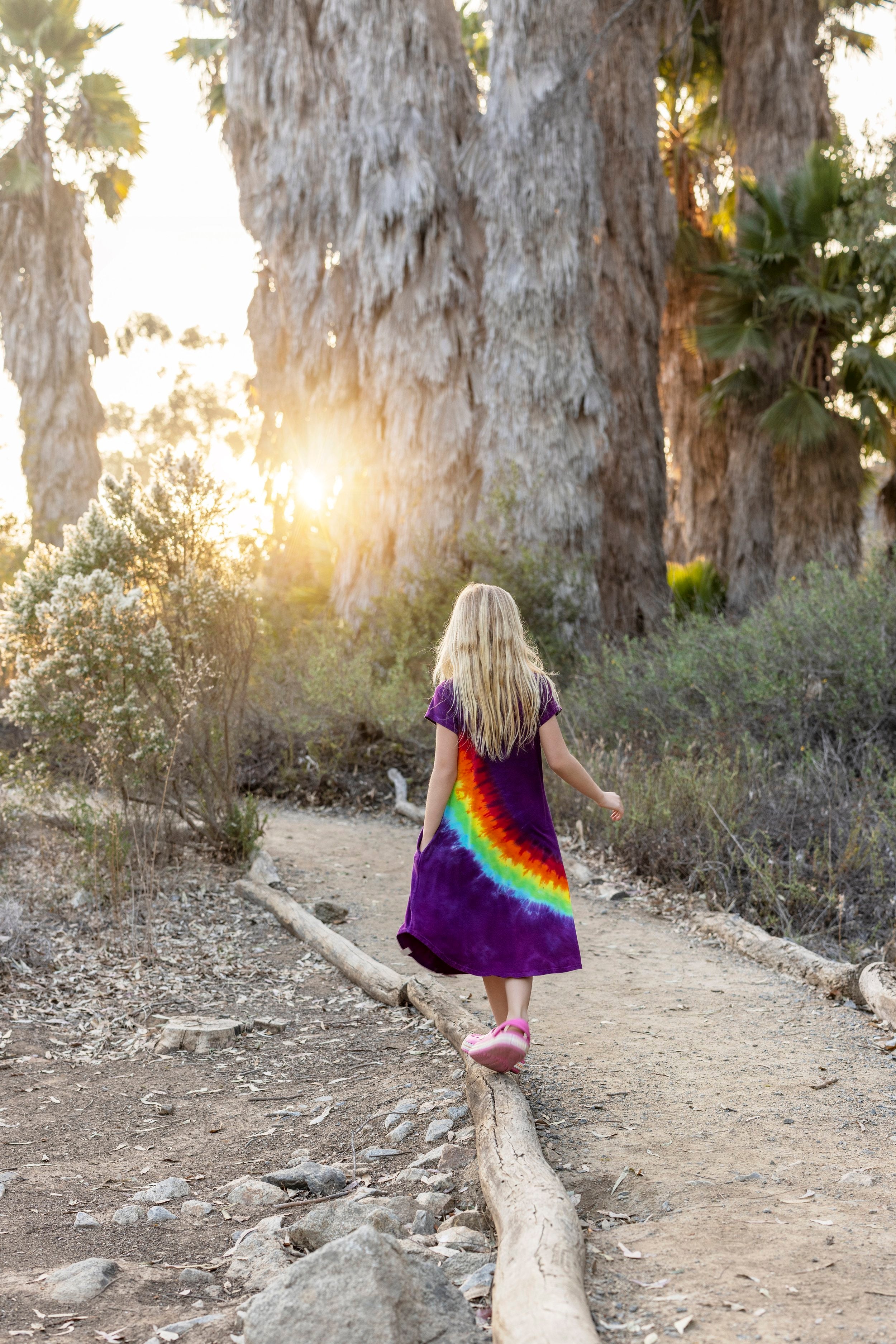 girl in a rainbow dress walking on a log