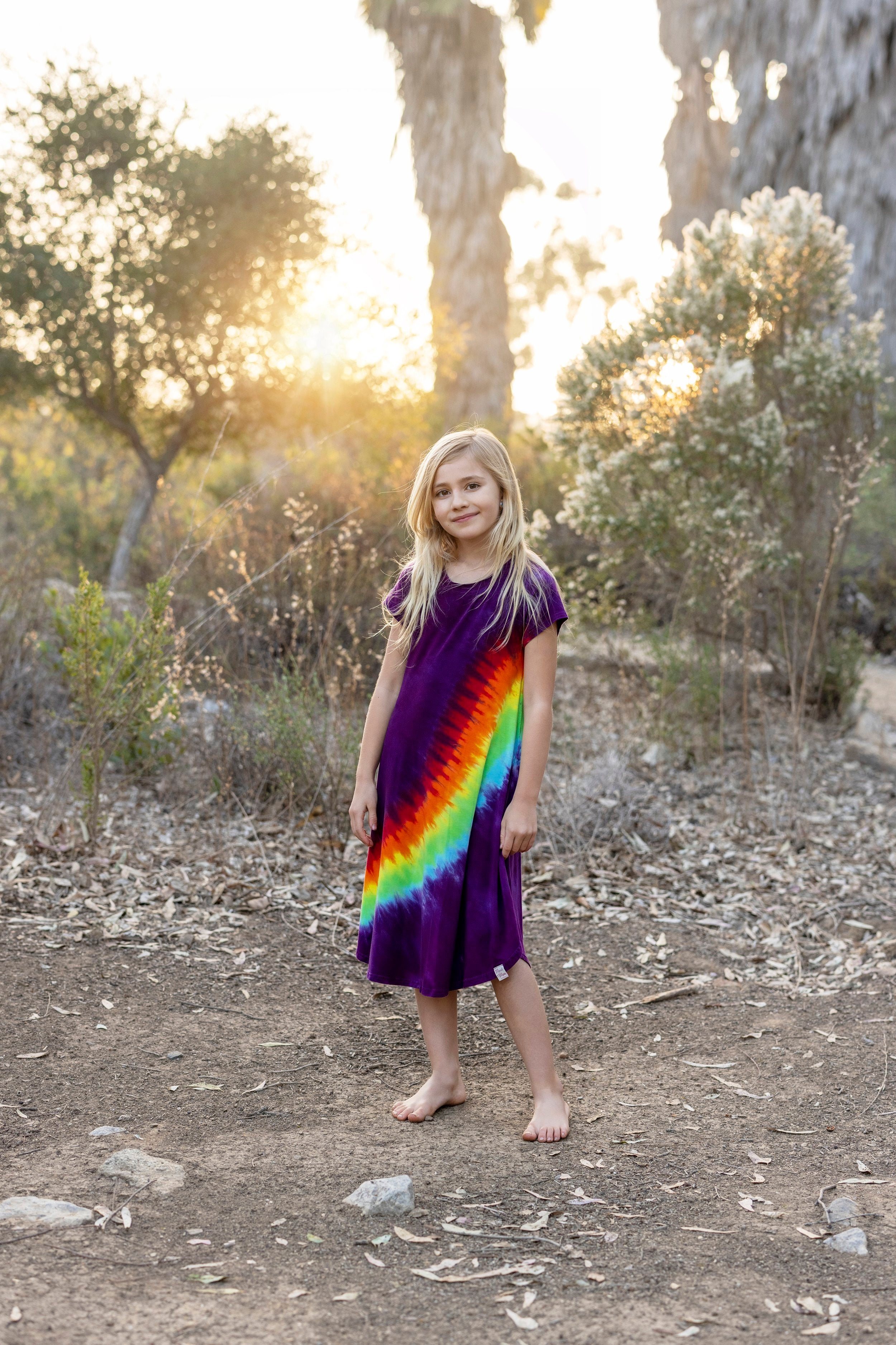 girl in rainbow dress standing on a dirt path