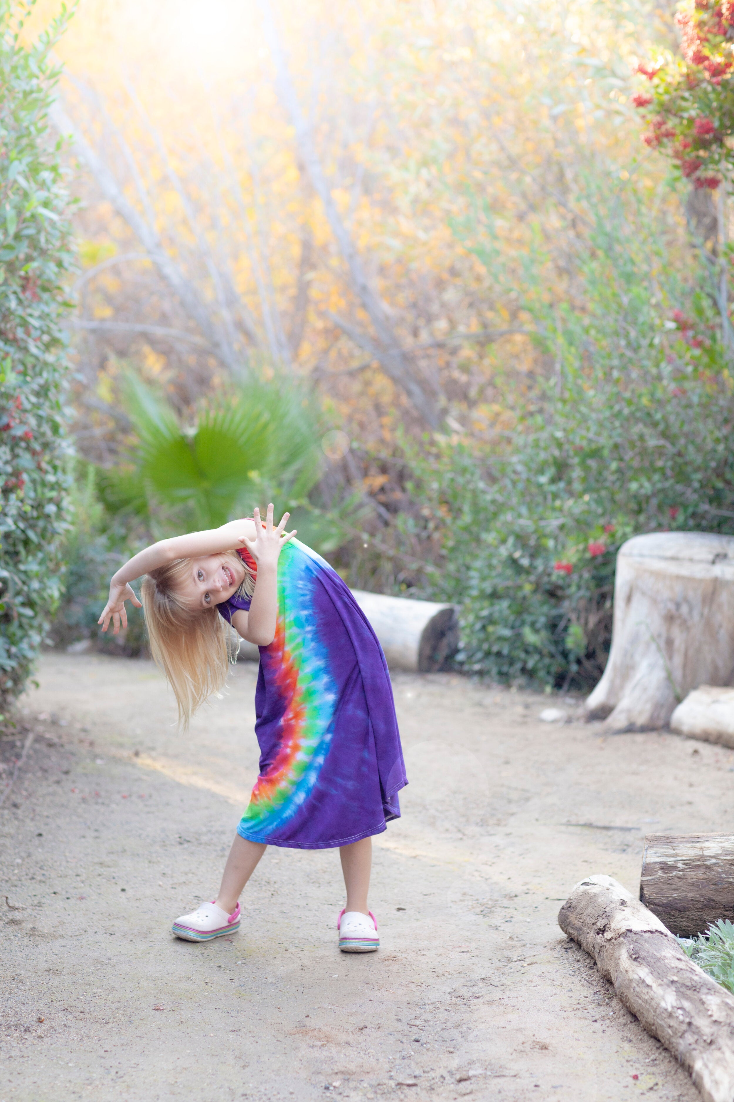 girl in rainbow dress leaning to the side with trees behind