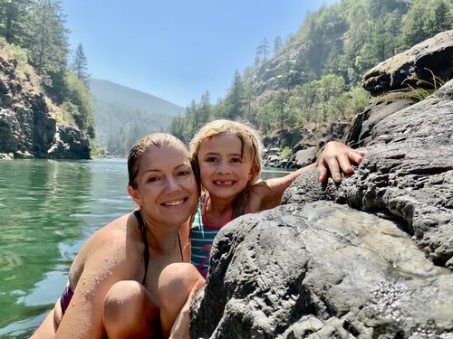 woman and child in a river with trees behind